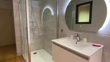 A modern bathroom with a glass shower enclosure, a white vanity with a mirror, and wooden flooring.