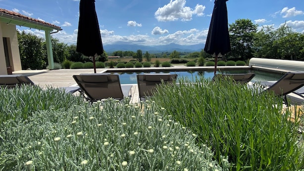 Ein Poolbereich mit Liegestühlen und Sonnenschirmen, umgeben von üppiger Vegetation und Blick auf ferne Berge.
