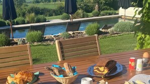 Ein Essplatz mit Brot, Kuchen und einer Tasse, mit Blick auf einen Pool und Berge.