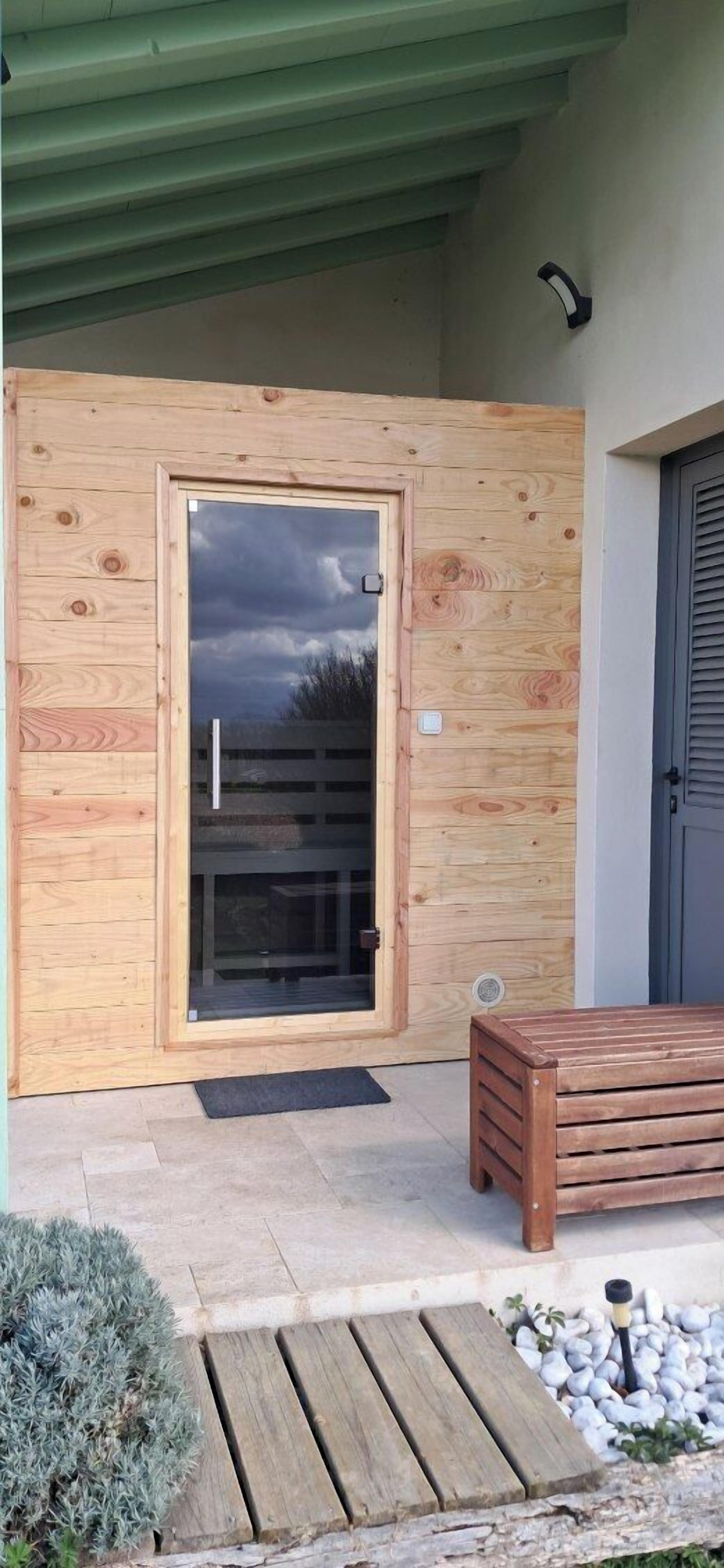 A wooden door with a glass panel, a bench, and a small garden area with pebbles and a plant.