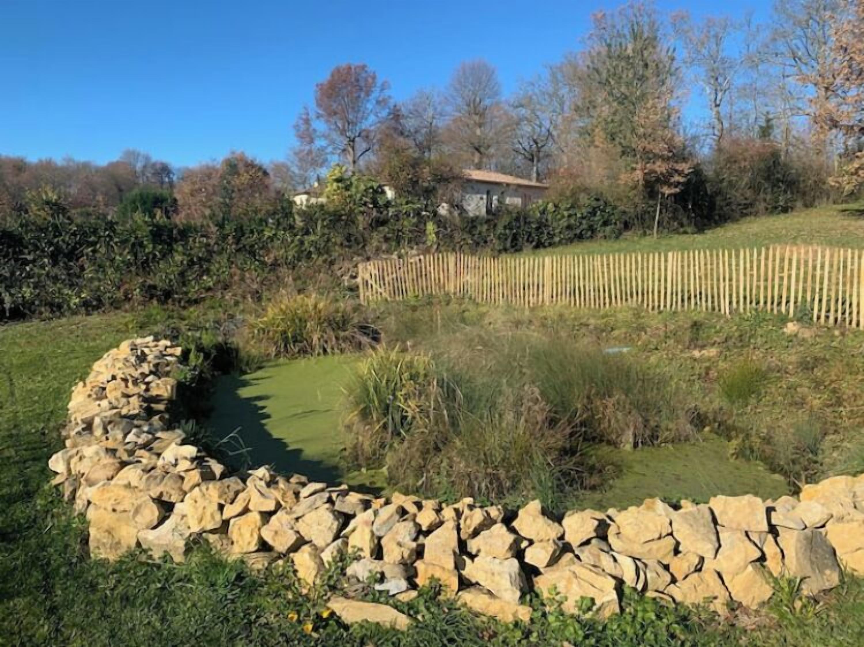Un muro de piedra, una cerca de madera y una casa en un entorno natural.