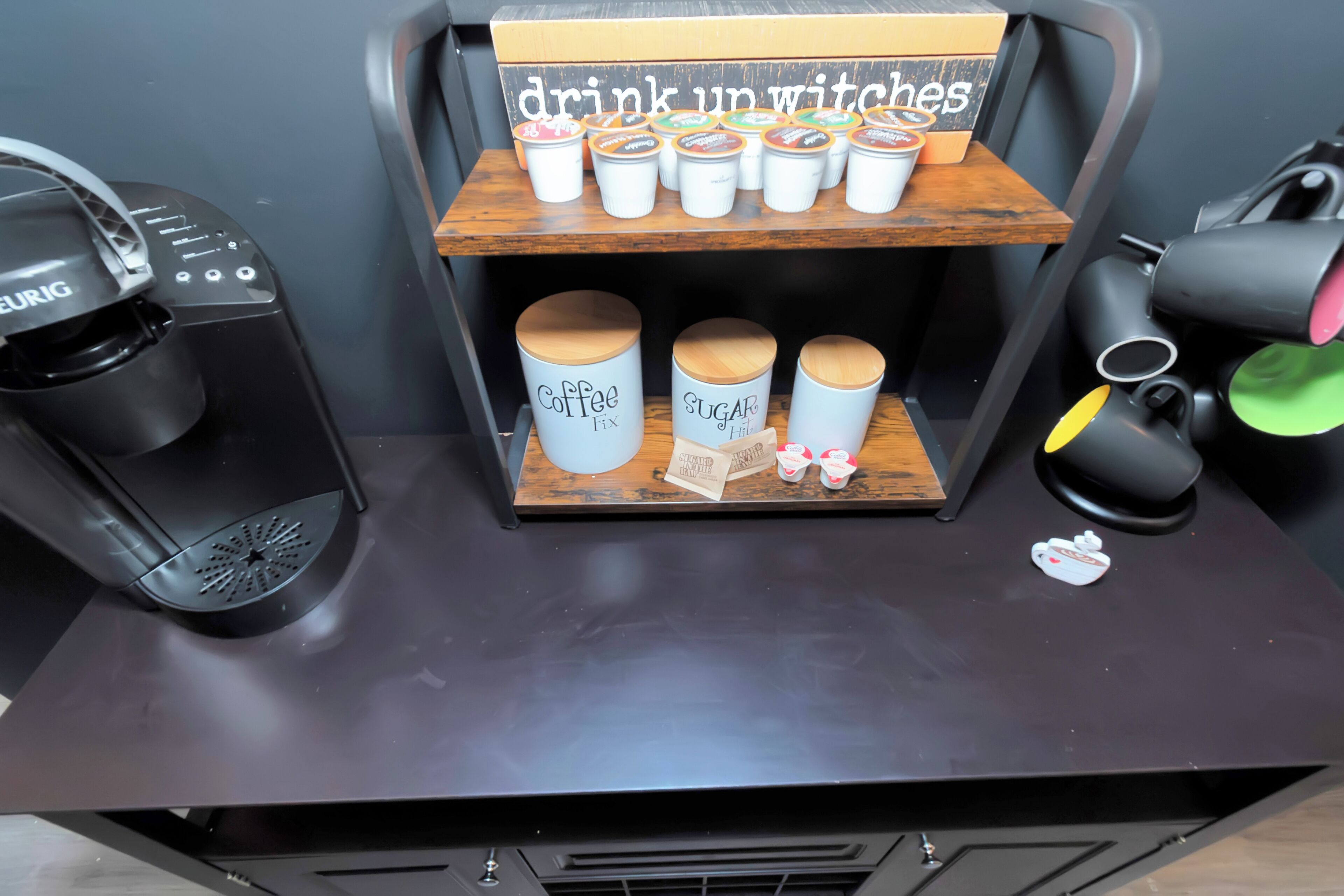 A coffee station with labeled containers for coffee and sugar, a coffee maker, and a sign that reads "drink up witches."