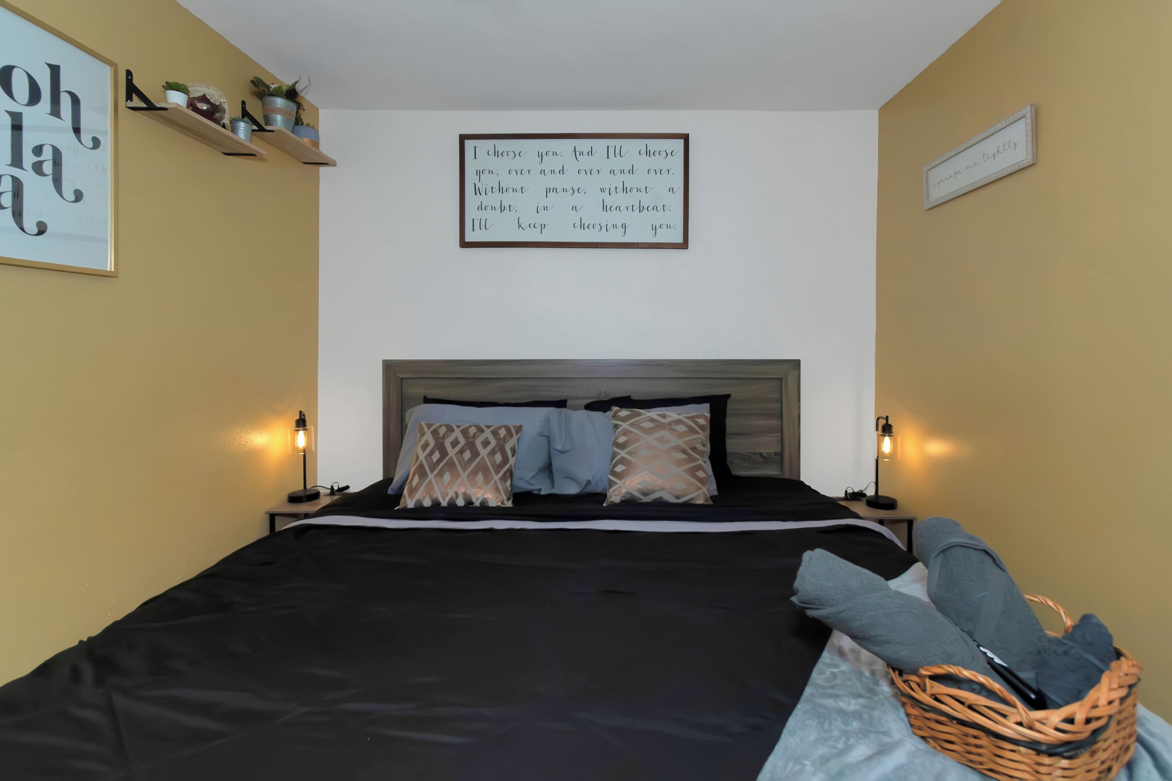 A neatly made bed with a black and white bedspread, two bedside lamps, and a wall with a framed inspirational quote.