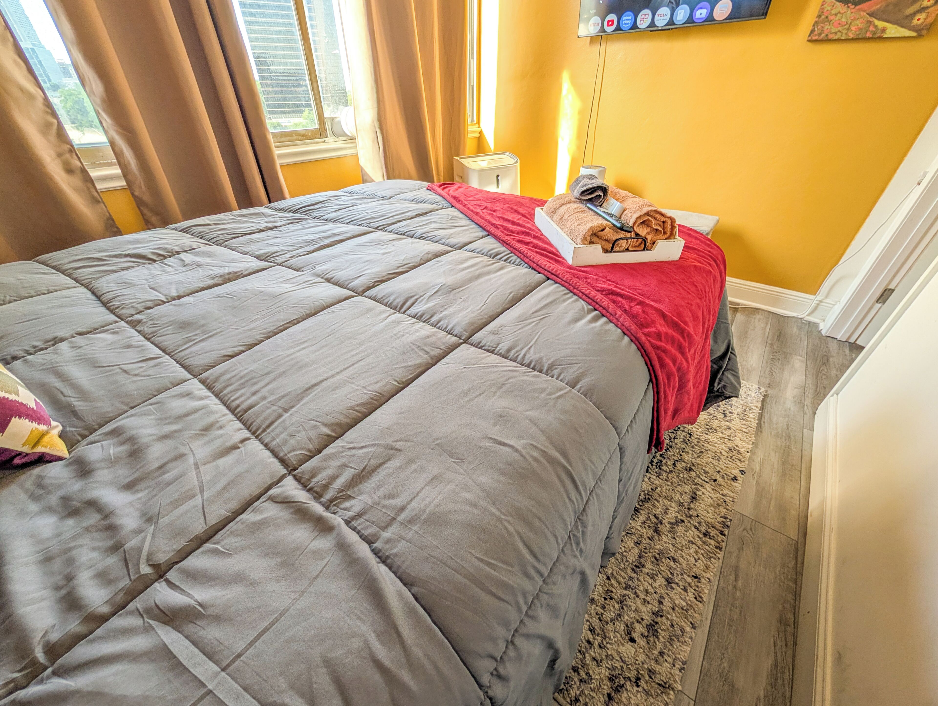 Un lit avec une couette grise, une couverture rouge et une boîte contenant des serviettes et une brosse à dents.