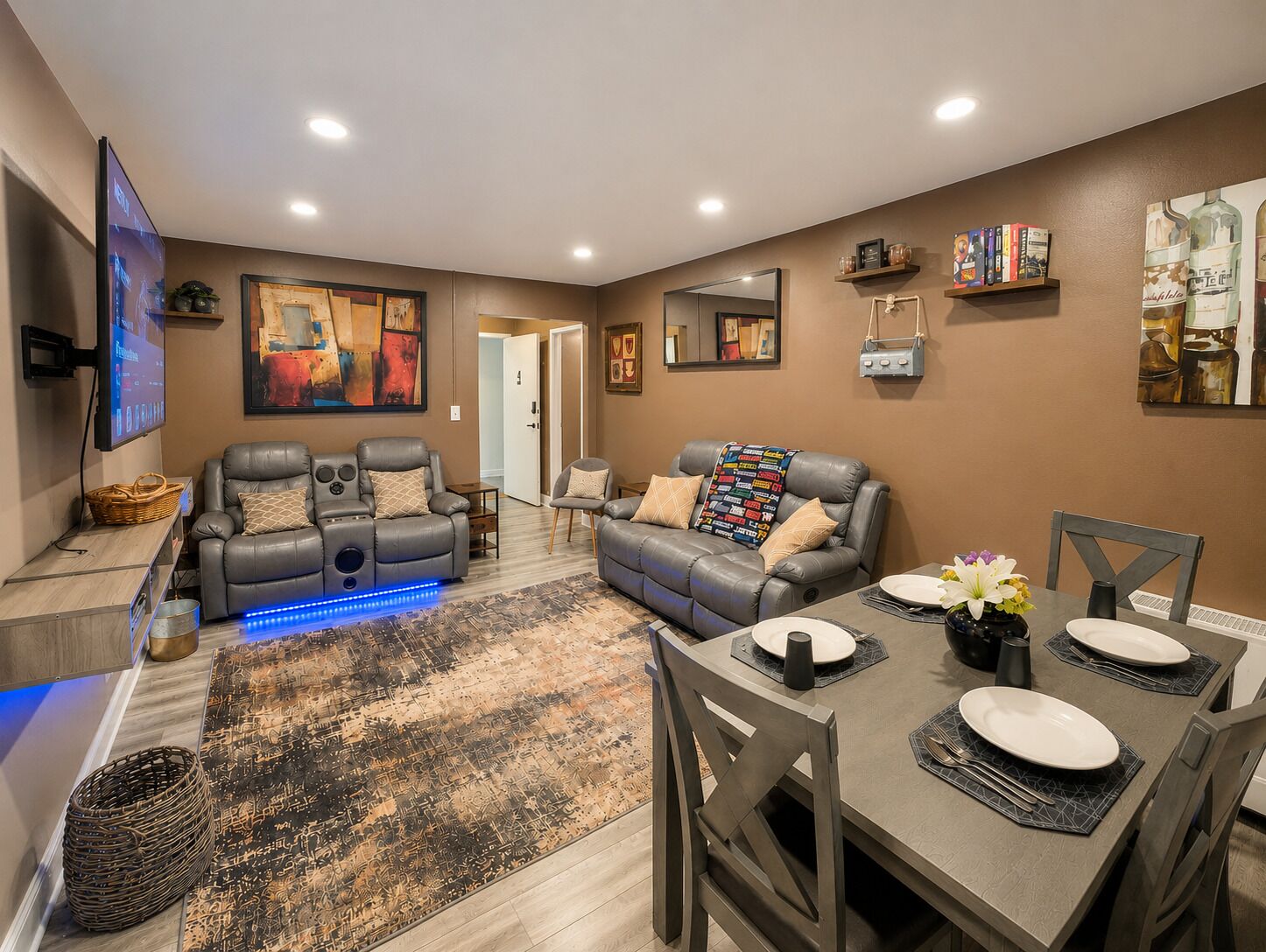 A modern living room with a gray leather sofa, a flat-screen TV, and a dining area with a table set for two.