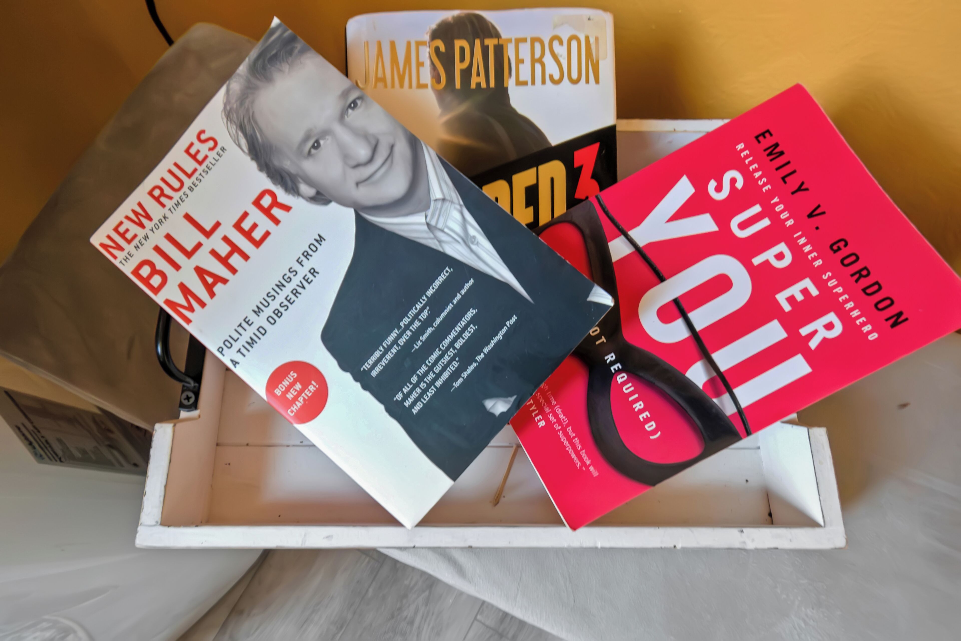 Un plateau blanc sur lequel reposent trois livres : « New Rules » de Bill Maher, « Red 3 » de James Patterson et « Super You » d’Emily V. Gordon.