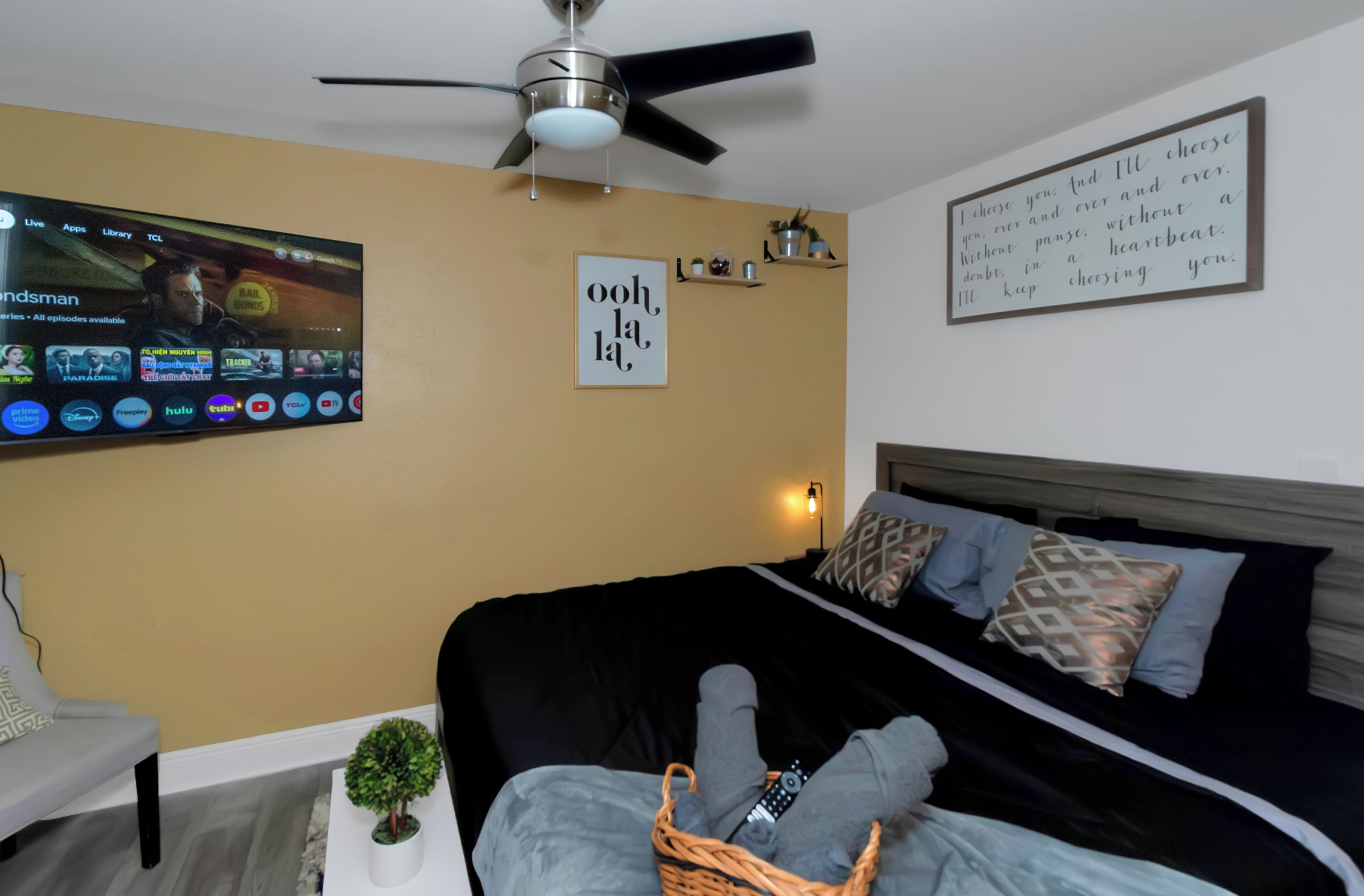 Ein Schlafzimmer mit einem Bett, einem an der Wand montierten Fernseher, einem Deckenventilator und einem motivierenden Zitat an der Wand.