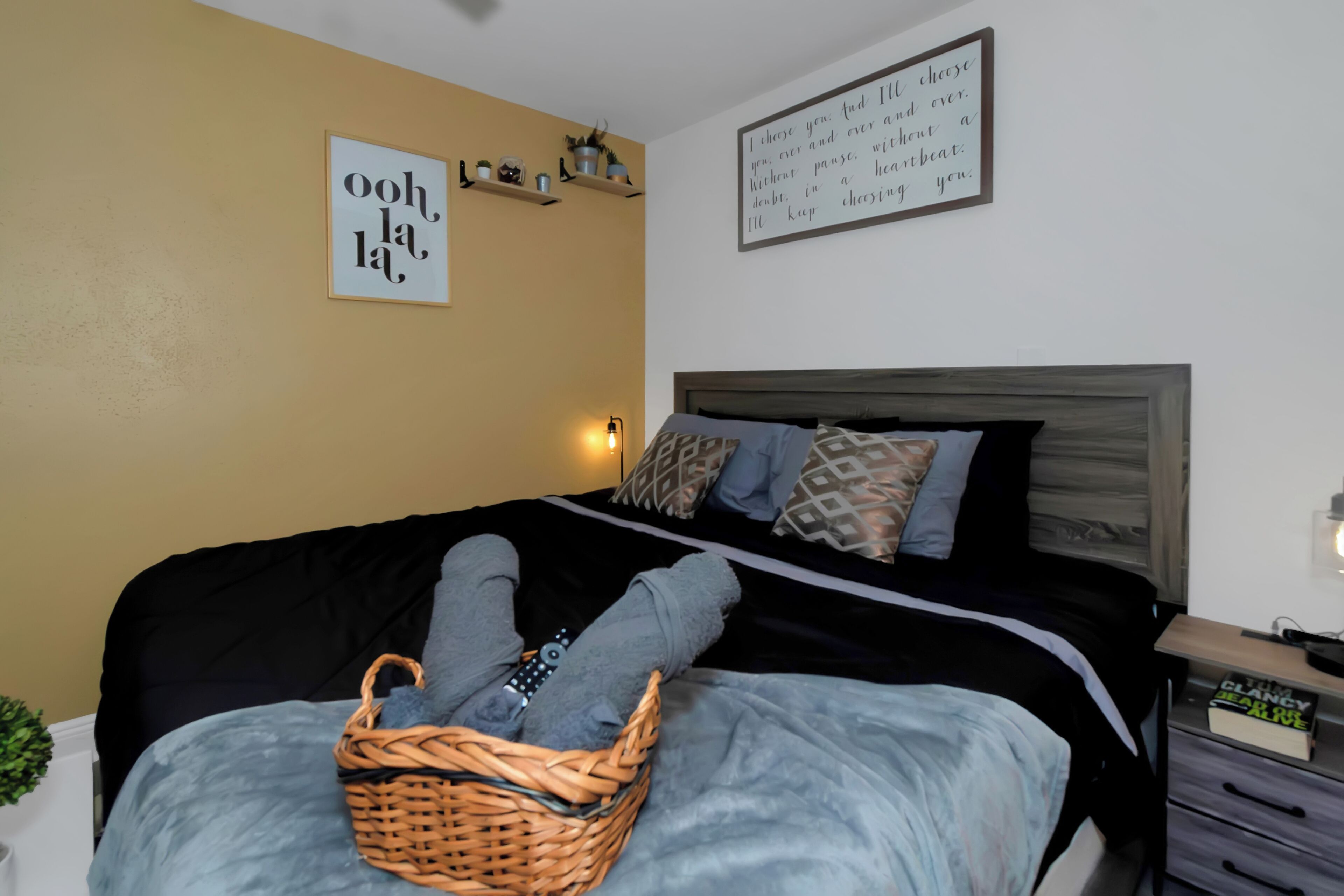 A bedroom with a bed, a bedside table with a lamp, and a wall with a motivational quote.