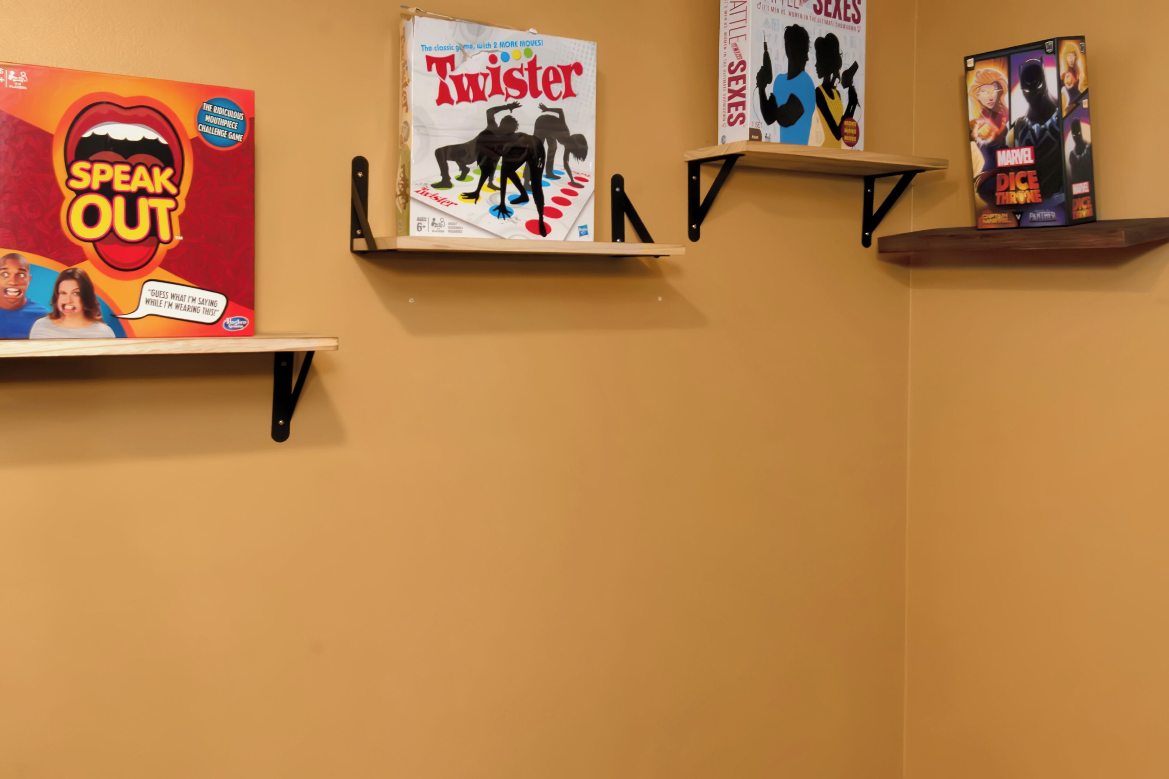 A wall with three shelves displaying various board games and a poster.