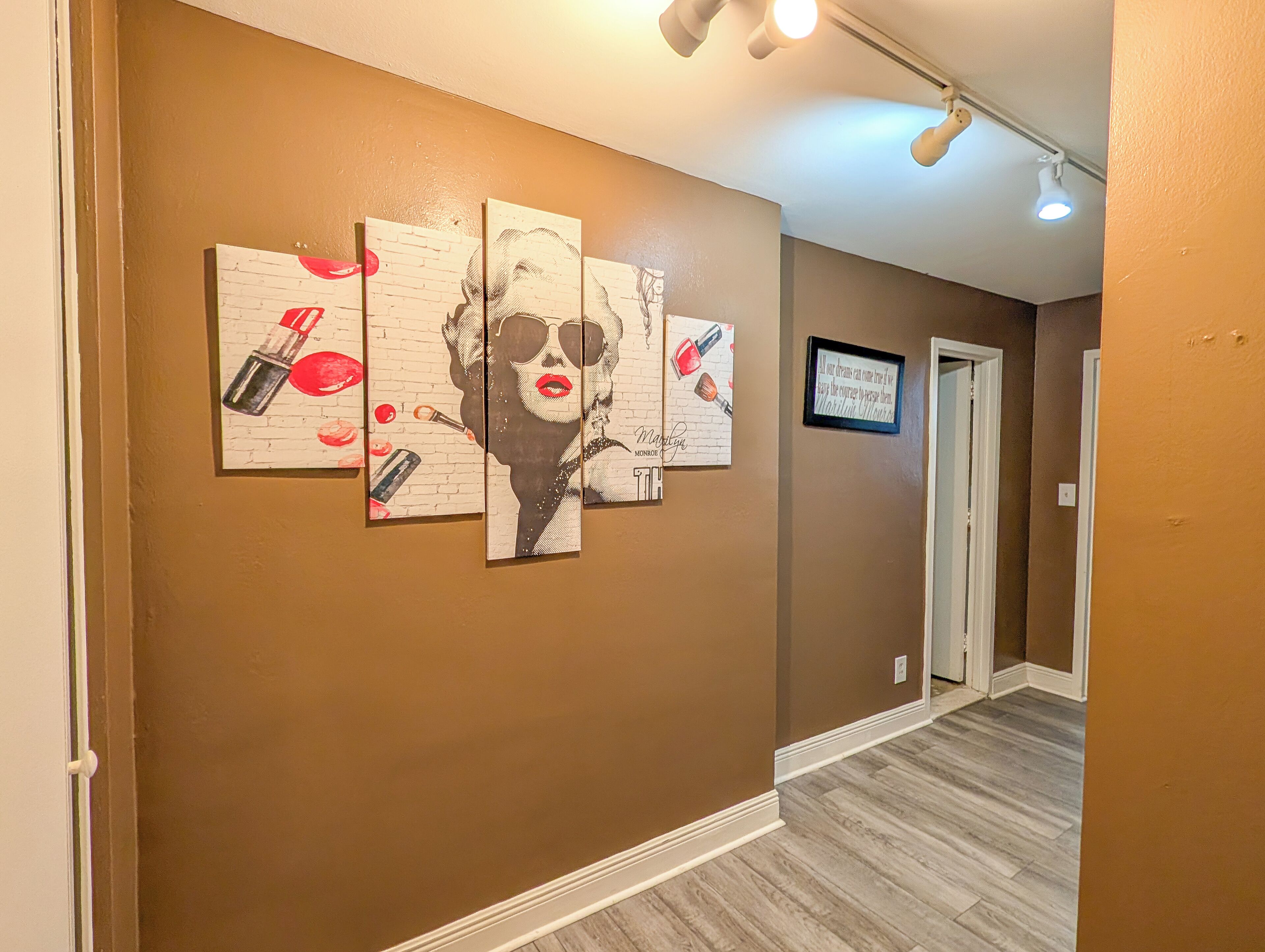A hallway with a brown wall, a series of framed artworks, and a door at the end.