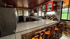 A kitchen with granite countertops, wooden chairs, and a stone wall.