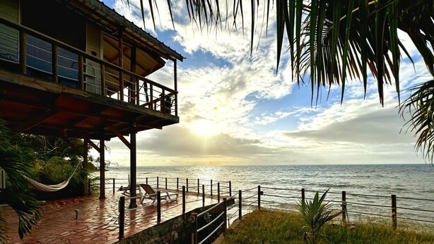 A wooden structure with a balcony overlooking the sea, a hammock, and a paved deck.