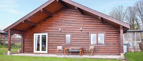 A log cabin with a pitched roof, a front porch with a table and chairs, and a sliding glass door.