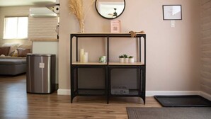 Un salon moderne avec un plancher en bois, une console en métal noir, un miroir et un tableau encadré accroché au mur.