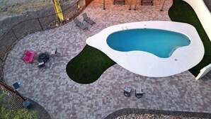 Une piscine à la forme originale, entourée d’une terrasse en briques avec des chaises longues et un espace salon abrité.