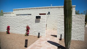 Un bâtiment à la façade en pierre blanche, un cactus et deux plantes à fleurs roses.