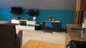 Una cucina compatta con un fornello, un'area pranzo con tavolo e sedie, una TV montata a parete e un piccolo angolo relax con un divano.