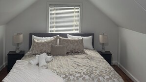 A bedroom with a sloped ceiling, a bed with a patterned duvet, two bedside tables with lamps, and a window with blinds.