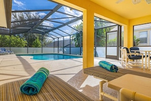 A pool area with a covered patio, lounge chairs, and a table with a rolled-up towel.