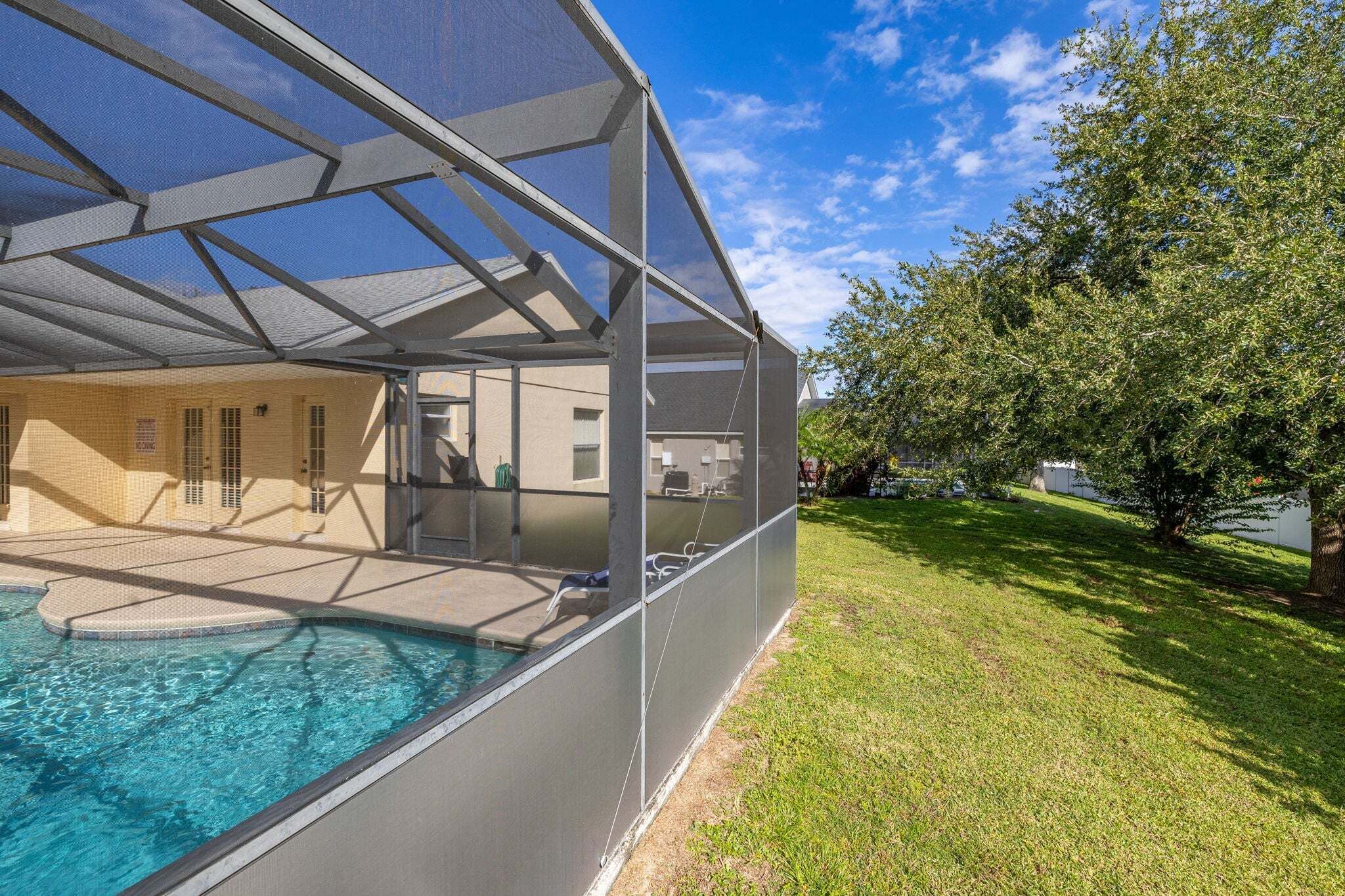 A swimming pool with a covered area, a grassy lawn, and a tree.