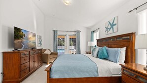 A bedroom with a wooden bed, a dresser, a nightstand, a lamp, and a painting of a beach scene.