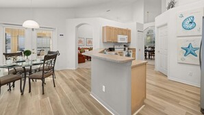 A modern kitchen with a central island, wooden cabinets, and a dining area with a glass table and chairs.