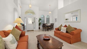 A spacious living room with two orange sofas, a wooden coffee table, and a dining area with a table and chairs.