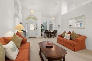 A spacious living room with two orange sofas, a wooden coffee table, and a dining area with a table and chairs.