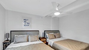 Une chambre d’hôtel avec deux lits, un ventilateur de plafond, une table de chevet et un panneau mural sur lequel on peut lire : « RENDEZ-VOUS À LA PLAGE ».