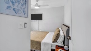Un dormitori amb un llit, un ventilador de sostre, un televisor penjat a la paret i una làmpada fixada a la paret.