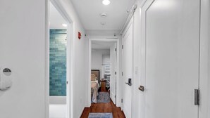 Un couloir aux murs blancs, avec un tapis bleu et un mur recouvert de carreaux sur le côté gauche.