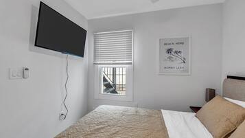 A bedroom with a bed, a TV mounted on the wall, a window with blinds, and a poster on the wall.