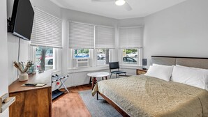 Une chambre d’hôtel équipée d’un lit, d’un bureau, d’une chaise, d’une télévision et de fenêtres avec des stores.
