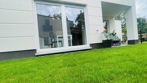 A modern house with a large sliding glass door, a well-maintained lawn, and a potted plant on the porch.