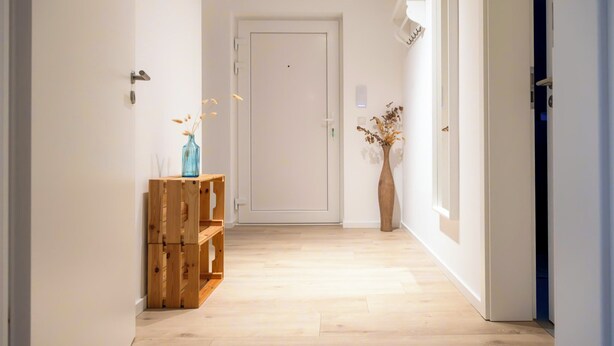 A hallway with a wooden bench, a vase with dried flowers, and a white door at the end.