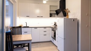 A modern kitchen with white cabinets, a black range hood, a white refrigerator, and a dining area with a wooden table and chairs.