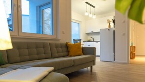 A modern living room with a sofa, a dining area, and a kitchen in the background.