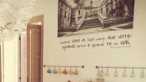 A cozy room with a red table displaying various food items and a wall with a quote in Italian. - B&B LA TUA DIMORA (Palermo)