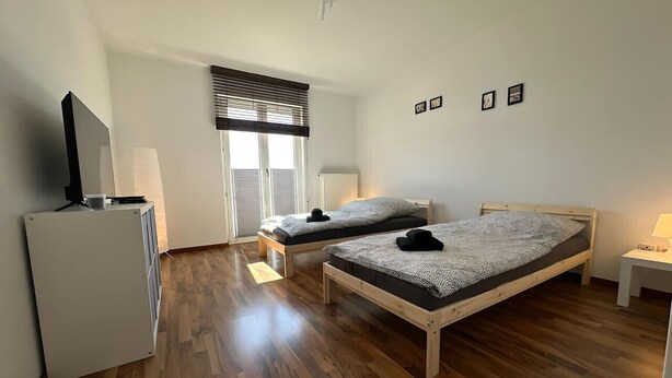 A bedroom with two beds, a radiator, a TV, and a window with blinds.