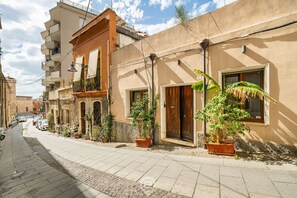 Una calle estrecha flanqueada por edificios de varios pisos, cada uno con balcones y plantas en macetas.
