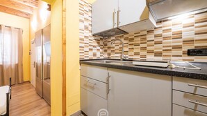 Een compacte keuken met een betegelde spatwand, roestvrijstalen apparatuur en een zwart aanrecht.