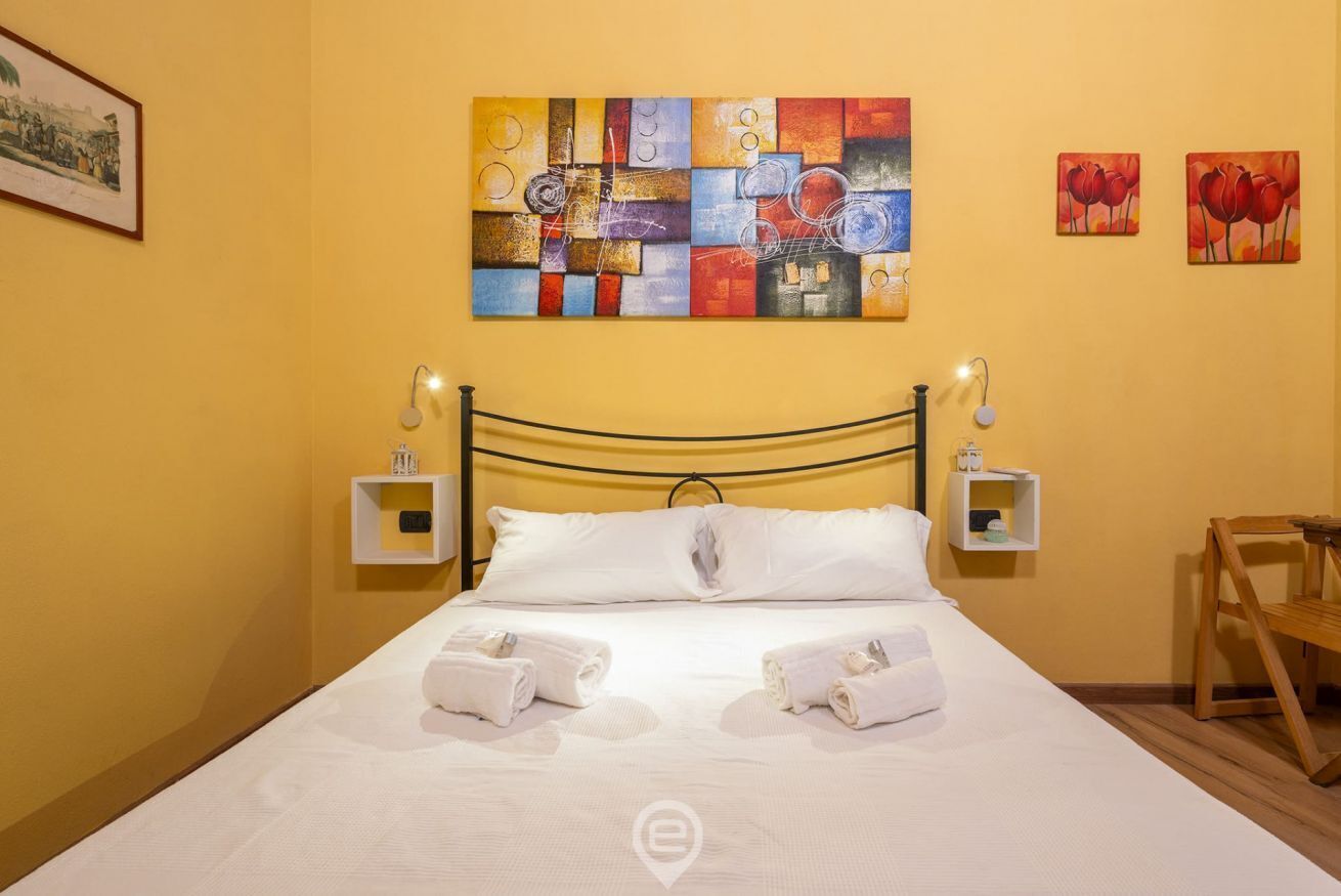 A hotel room with a bed, two bedside tables with lamps, a painting on the wall, and a chair.
