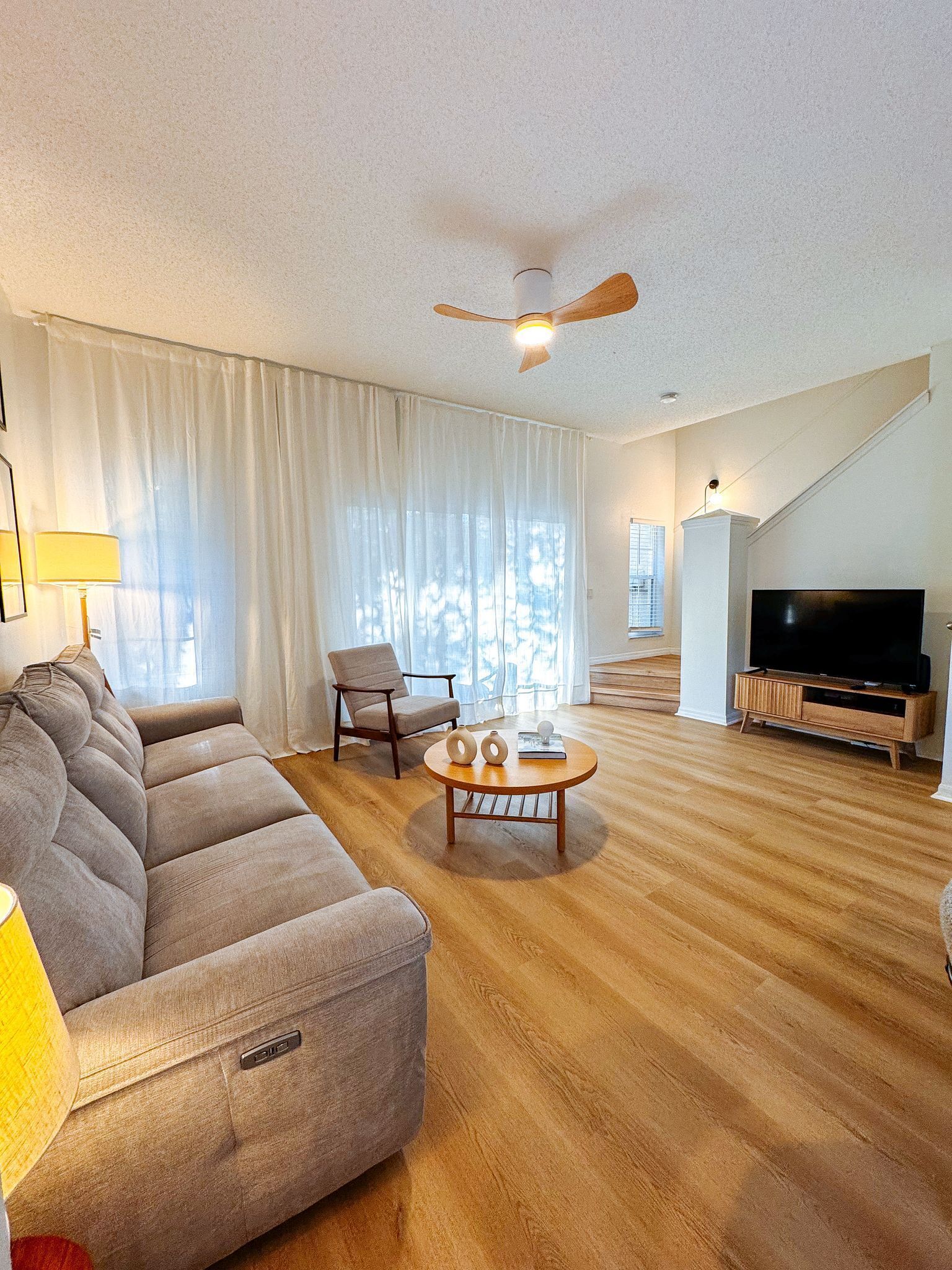 Ein Wohnzimmer mit einer Couch, einem Couchtisch, einem Sessel, einem Fernseher und einem Deckenventilator.