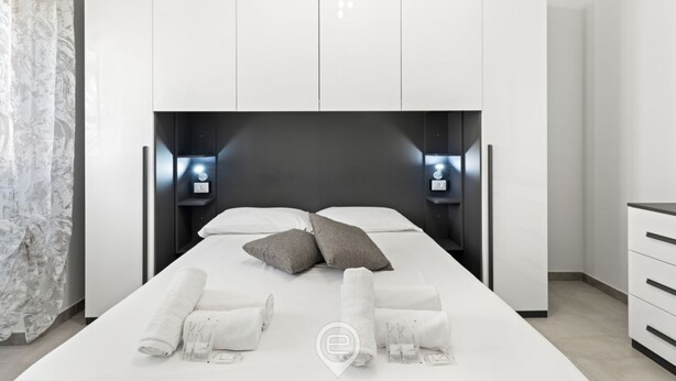 Una habitación de hotel moderna con una cama grande, ropa de cama blanca, un cabecero oscuro y dos lámparas de noche.
