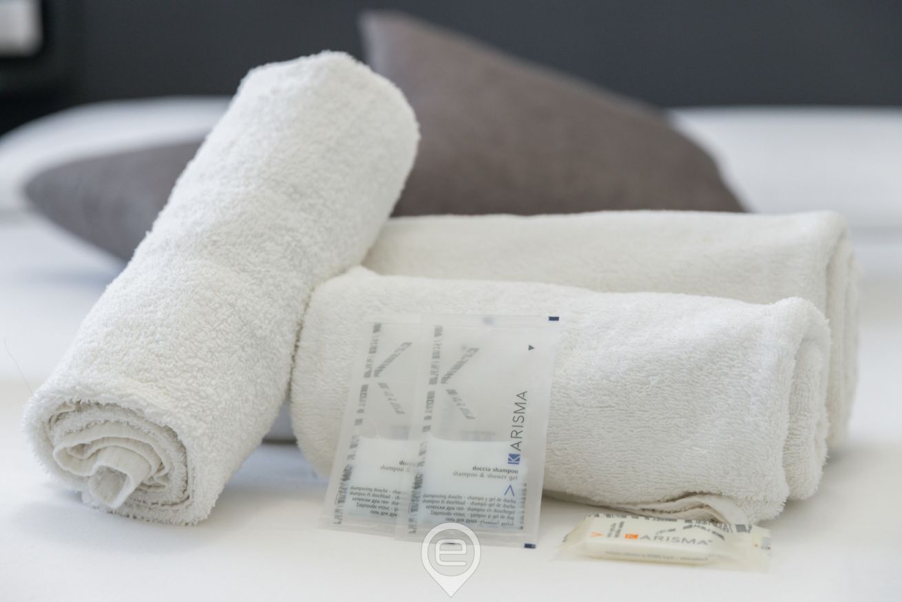 A neatly folded white towel and a bar of soap on a bed with a pillow.