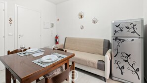 Un comedor con una mesa de madera dispuesta para dos personas, un sofá color beige y un refrigerador adornado con enredaderas.