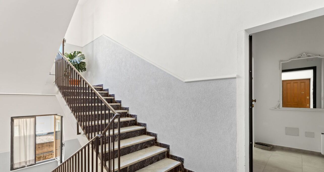 A modern staircase with a metal railing, white walls, and a view of the outside.