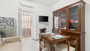 Un comedor con una mesa de madera dispuesta para cuatro, un televisor montado en la pared y un aparador con puertas de cristal.