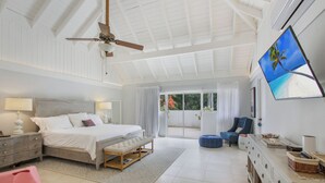 Un dormitorio amplio con una cama grande, ventilador de techo, televisión y vistas al exterior.