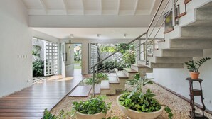 Un interior moderno con piso de madera, una escalera con barandillas de metal y plantas en macetas.